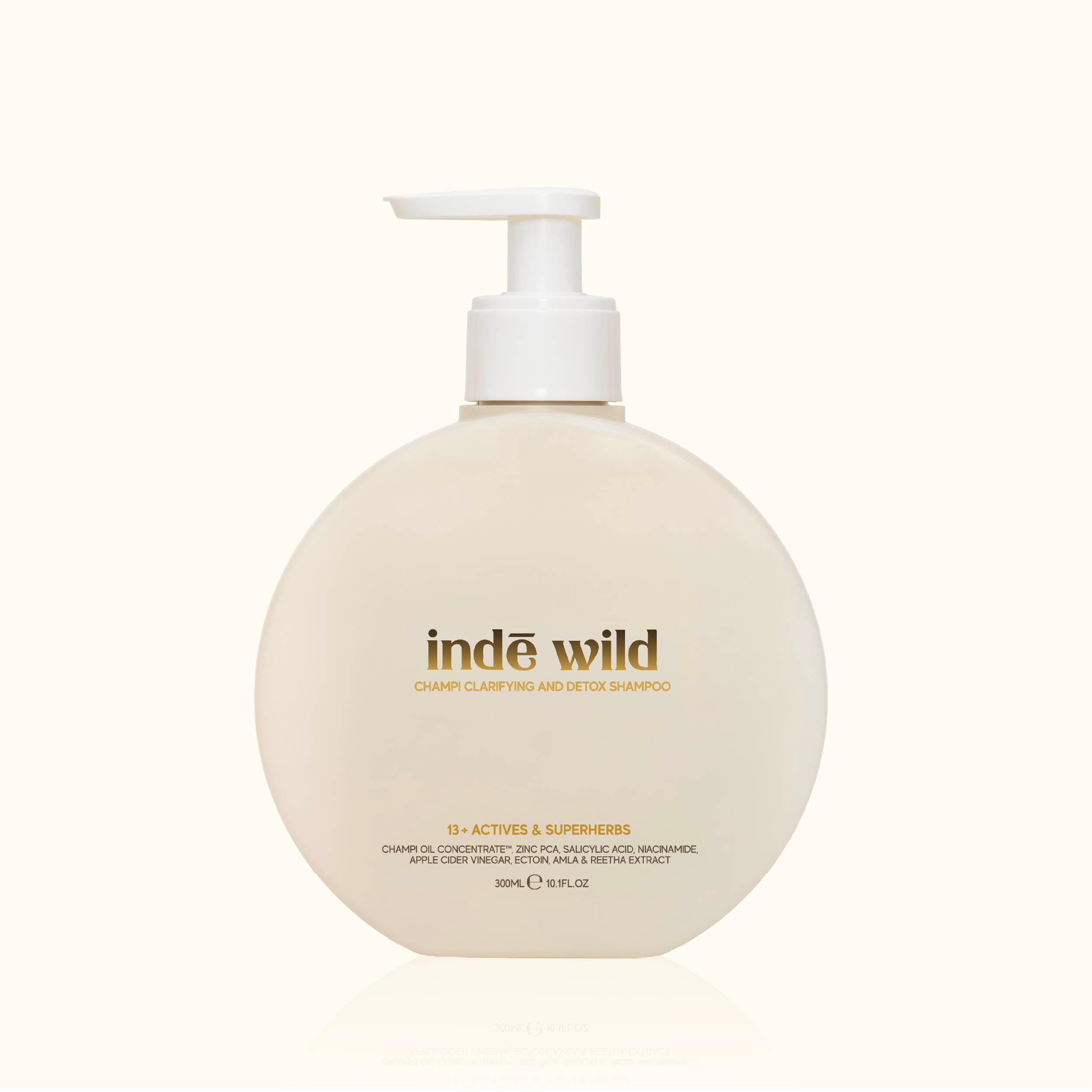 A round, off-white pump bottle of 'inde wild' shampoo with gold lettering, set against a solid cream background.
